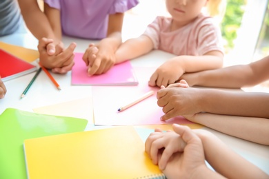 Little children holding hands at table, closeup. Unity concept