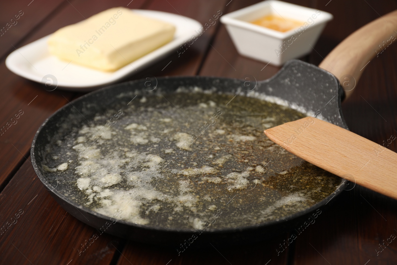 Photo of Melted butter in frying pan and spatula on wooden table, closeup