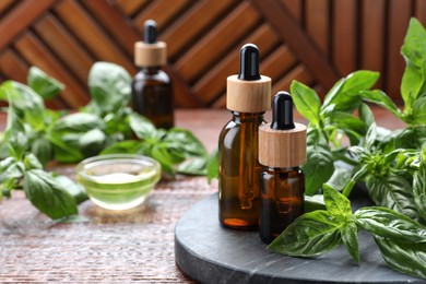 Bottles of basil essential oil and fresh leaves on wooden table, space for text