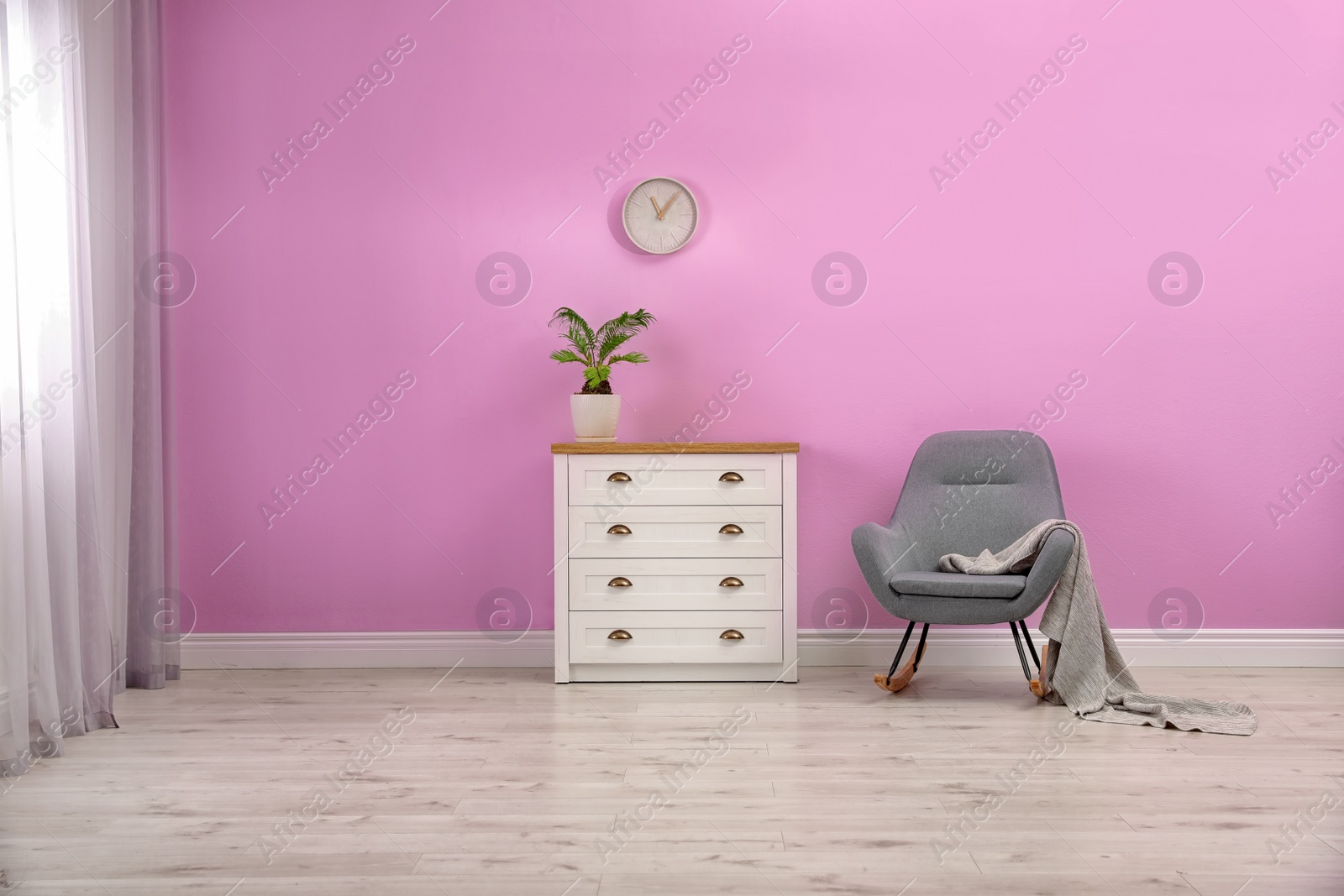 Photo of Stylish room interior with chest of drawers and rocking chair near color wall