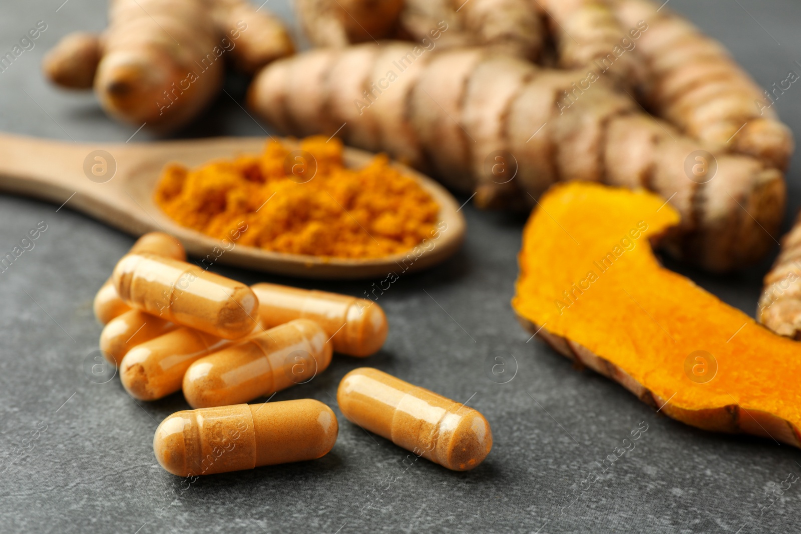 Photo of Turmeric roots and pills on grey table, closeup. Space for text