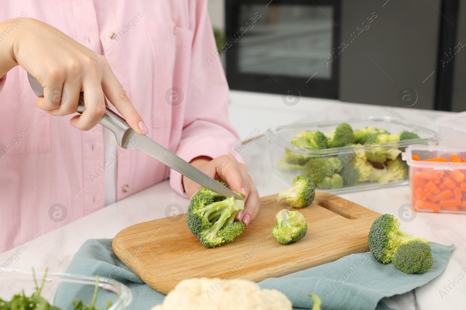 Photo of Woman cutting green broccoli near containers with fresh products at white marble table in kitchen, closeup