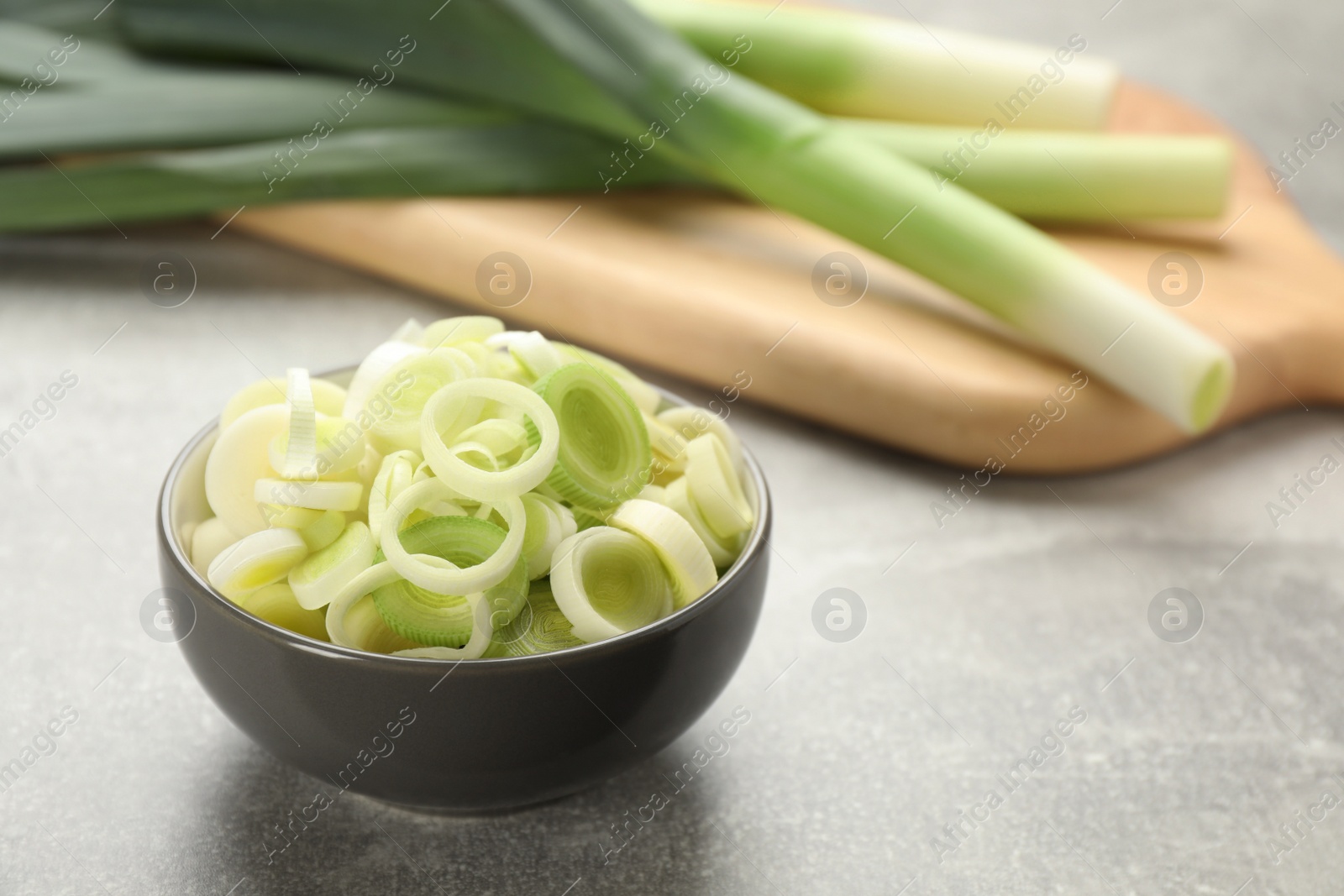 Photo of Cut fresh raw leek in bowl on grey table, space for text