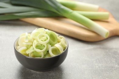 Photo of Cut fresh raw leek in bowl on grey table, space for text