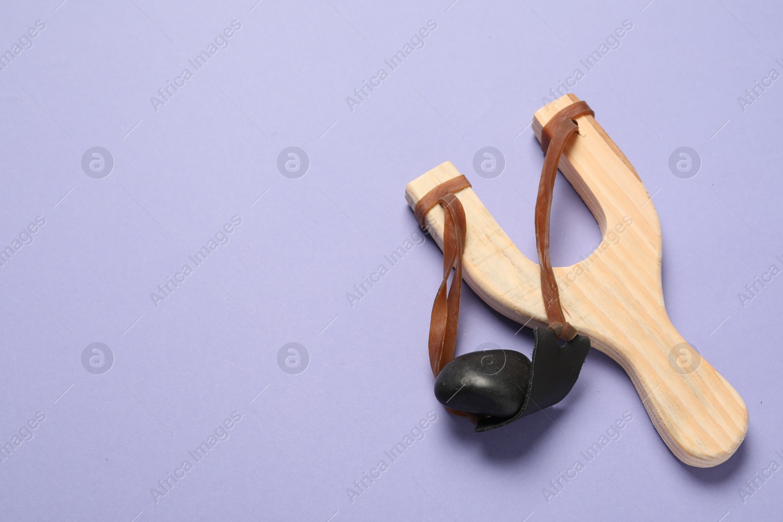 Photo of Wooden slingshot with pebble on violet background, top view. Space for text