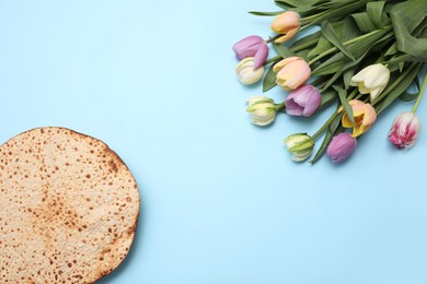Photo of Tasty matzo and fresh tulips on light blue background, flat lay with space for text. Passover (Pesach) celebration