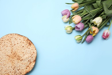 Tasty matzo and fresh tulips on light blue background, flat lay with space for text. Passover (Pesach) celebration