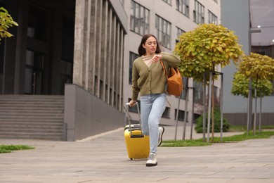 Photo of Being late. Worried woman with suitcase and backpack looking at watch while running outdoors
