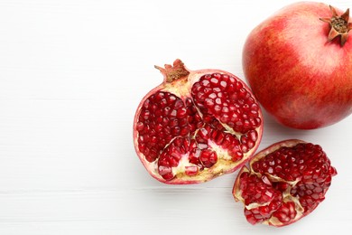 Photo of Fresh pomegranates on white wooden table, top view. Space for text