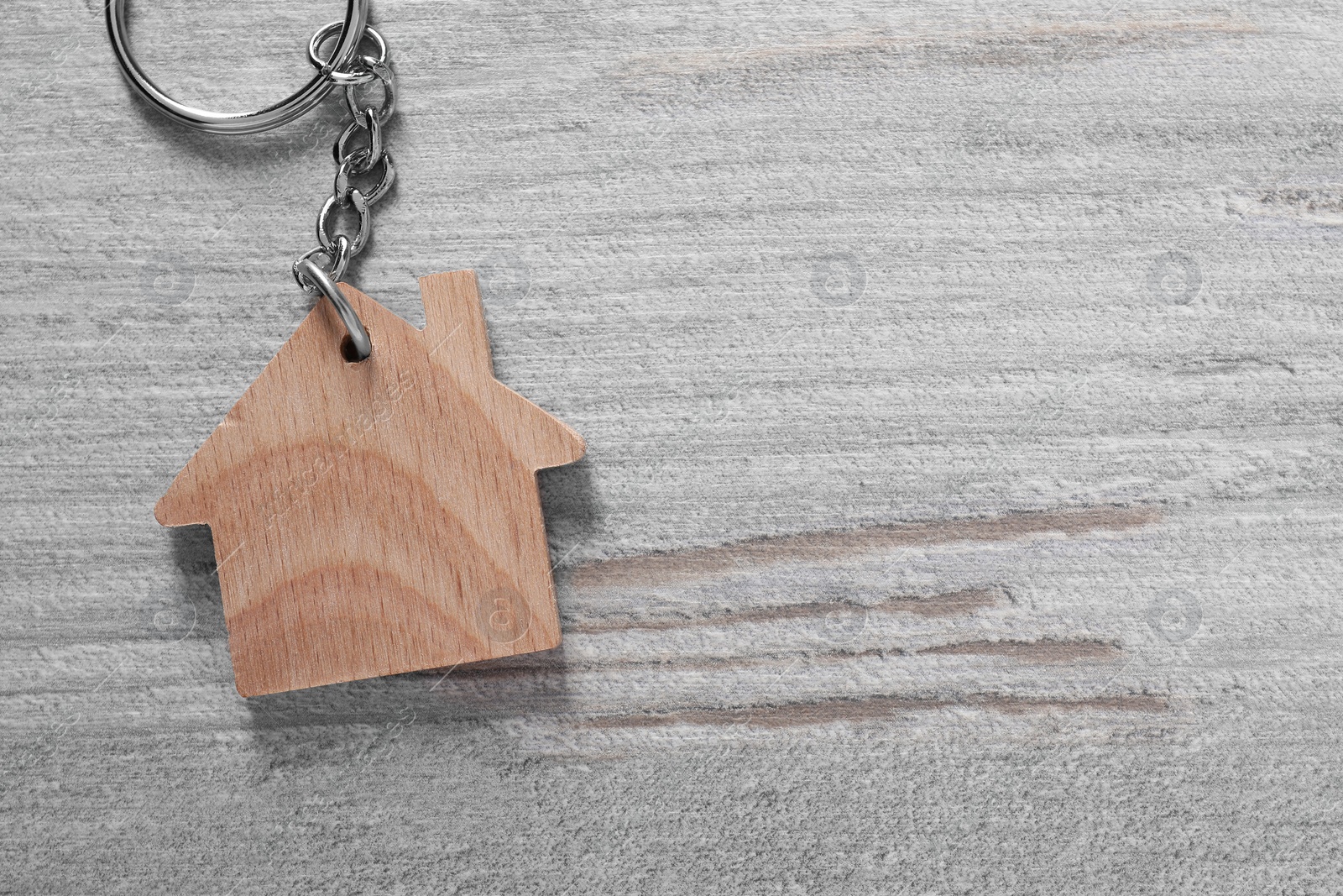 Photo of One keychain in shape of house on light wooden table, top view. Space for text