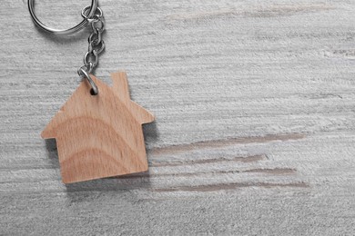 Photo of One keychain in shape of house on light wooden table, top view. Space for text