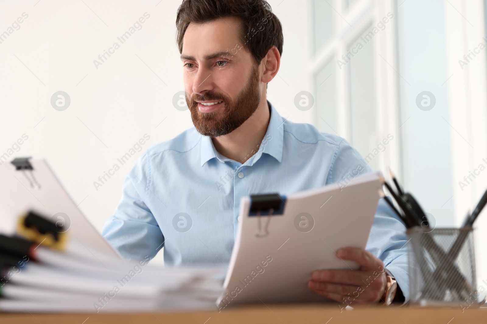 Photo of Happy businessman working with documents at wooden table in office