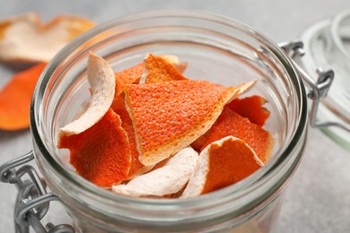 Glass jar with dry orange peels on light gray table, closeup