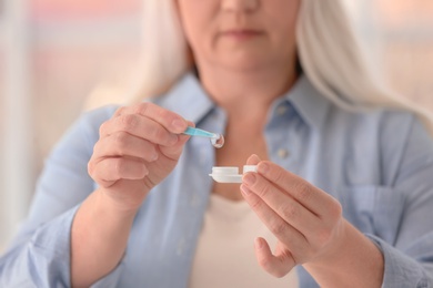 Senior woman taking contact lens from container, closeup of hands