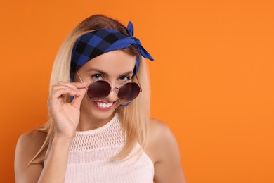 Photo of Portrait of smiling hippie woman in sunglasses on orange background. Space for text