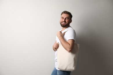 Photo of Happy young man with eco bag on light background. Space for text