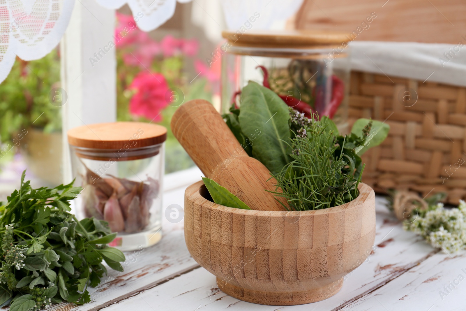 Photo of Mortar with pestle and fresh green herbs on white wooden table near window