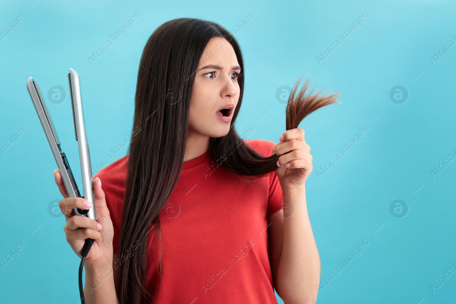 Photo of Upset woman with hair iron on blue background, space for text