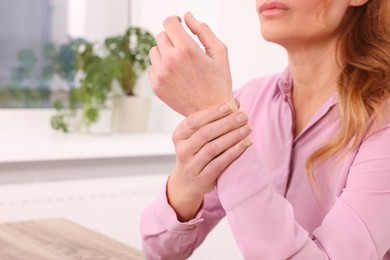 Photo of Woman suffering from pain in wrist at table indoors, closeup. Arthritis symptoms