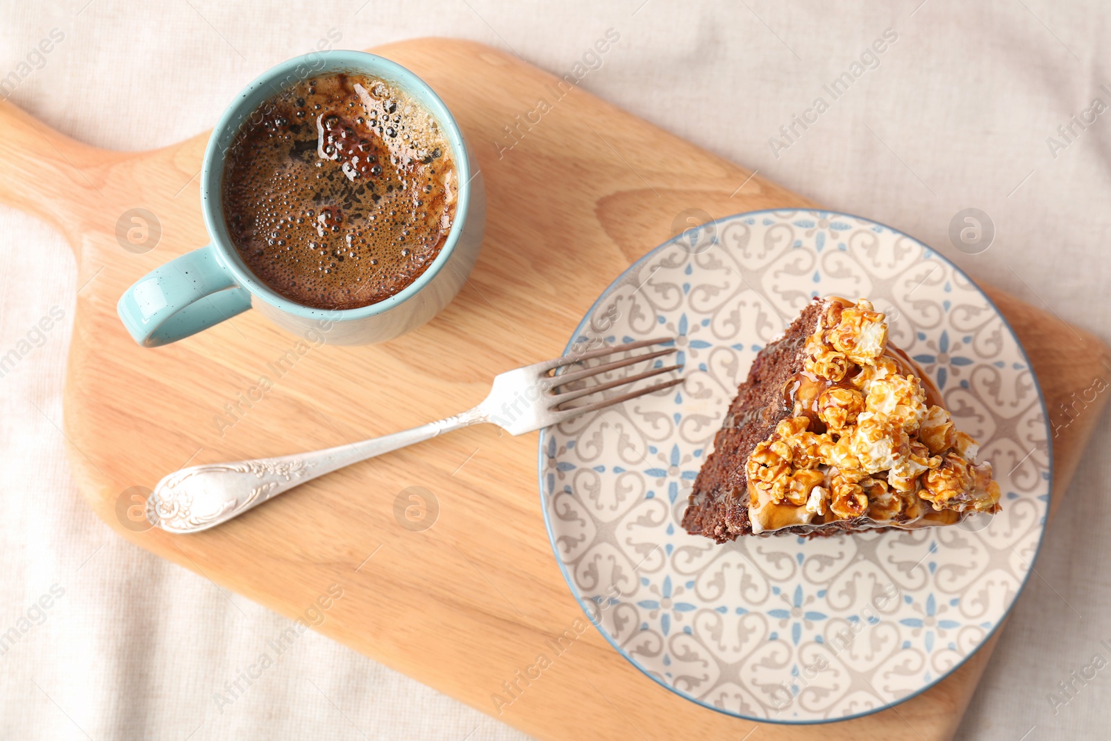 Photo of Piece of delicious homemade cake with caramel sauce and cup of coffee on wooden board, top view