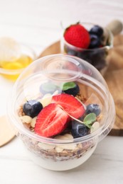 Photo of Tasty granola with berries, yogurt and almond flakes in plastic cup on white table, closeup