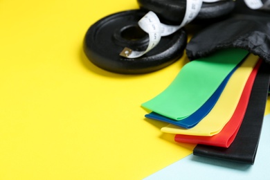 Photo of Fitness elastic bands, measuring tape and weight plates on color background, closeup. Space for text