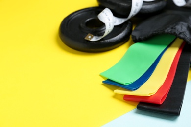 Fitness elastic bands, measuring tape and weight plates on color background, closeup. Space for text