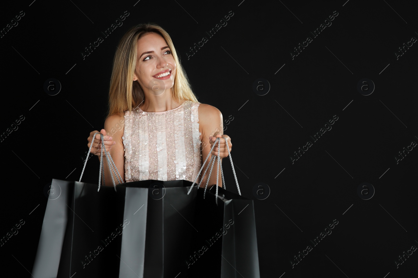 Photo of Happy young woman with shopping bags on dark background. Black Friday Sale