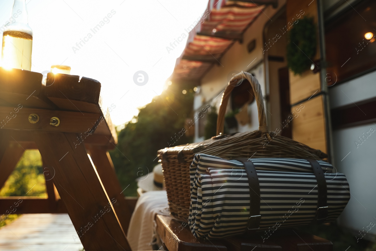 Photo of Wicker basket with picnic blanket on wooden bench near motorhome. Camping season