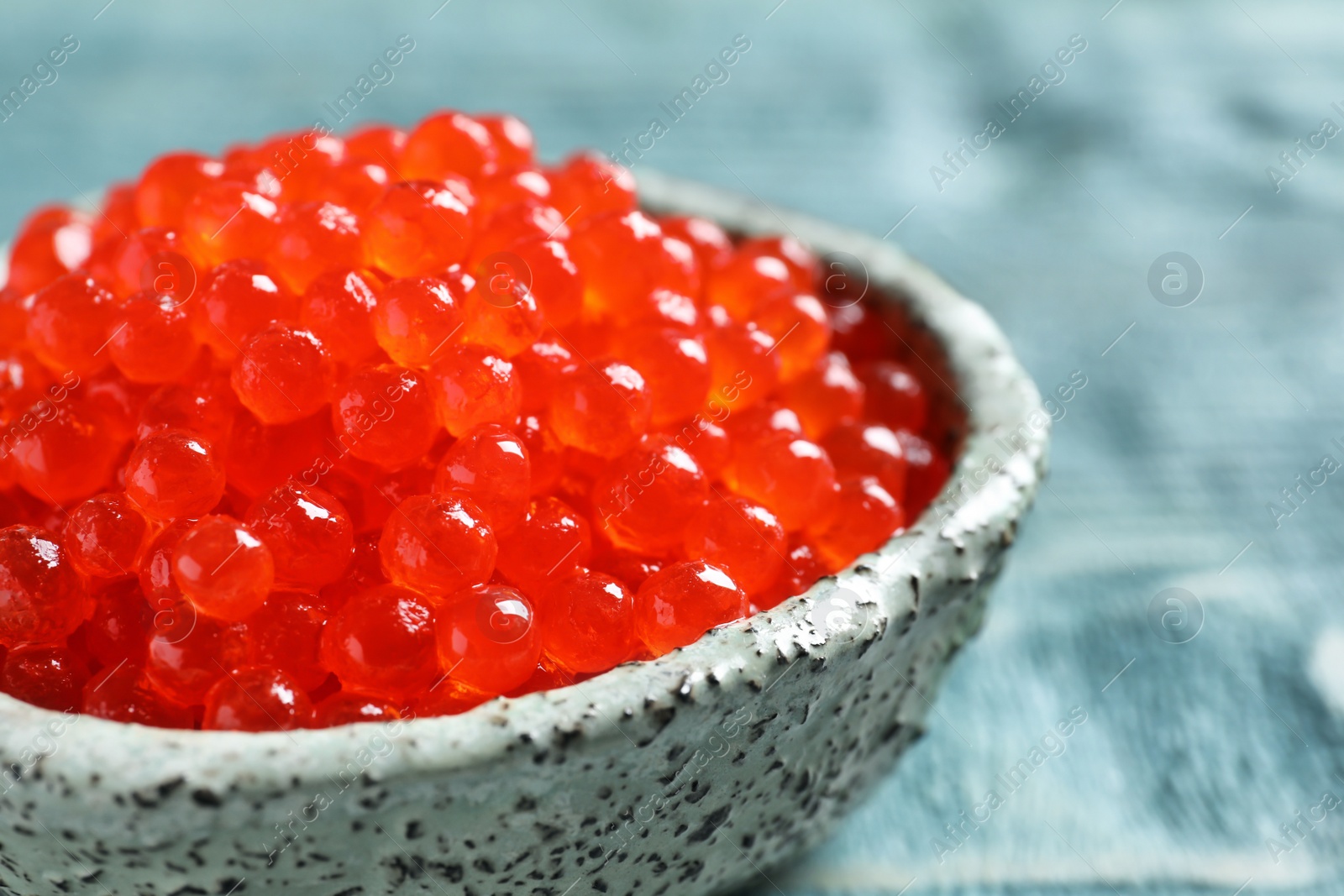 Photo of Ceramic bowl with delicious red caviar on table, closeup