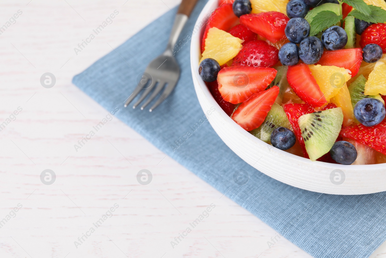 Photo of Delicious fresh fruit salad in bowl served on white wooden table, closeup. Space for text