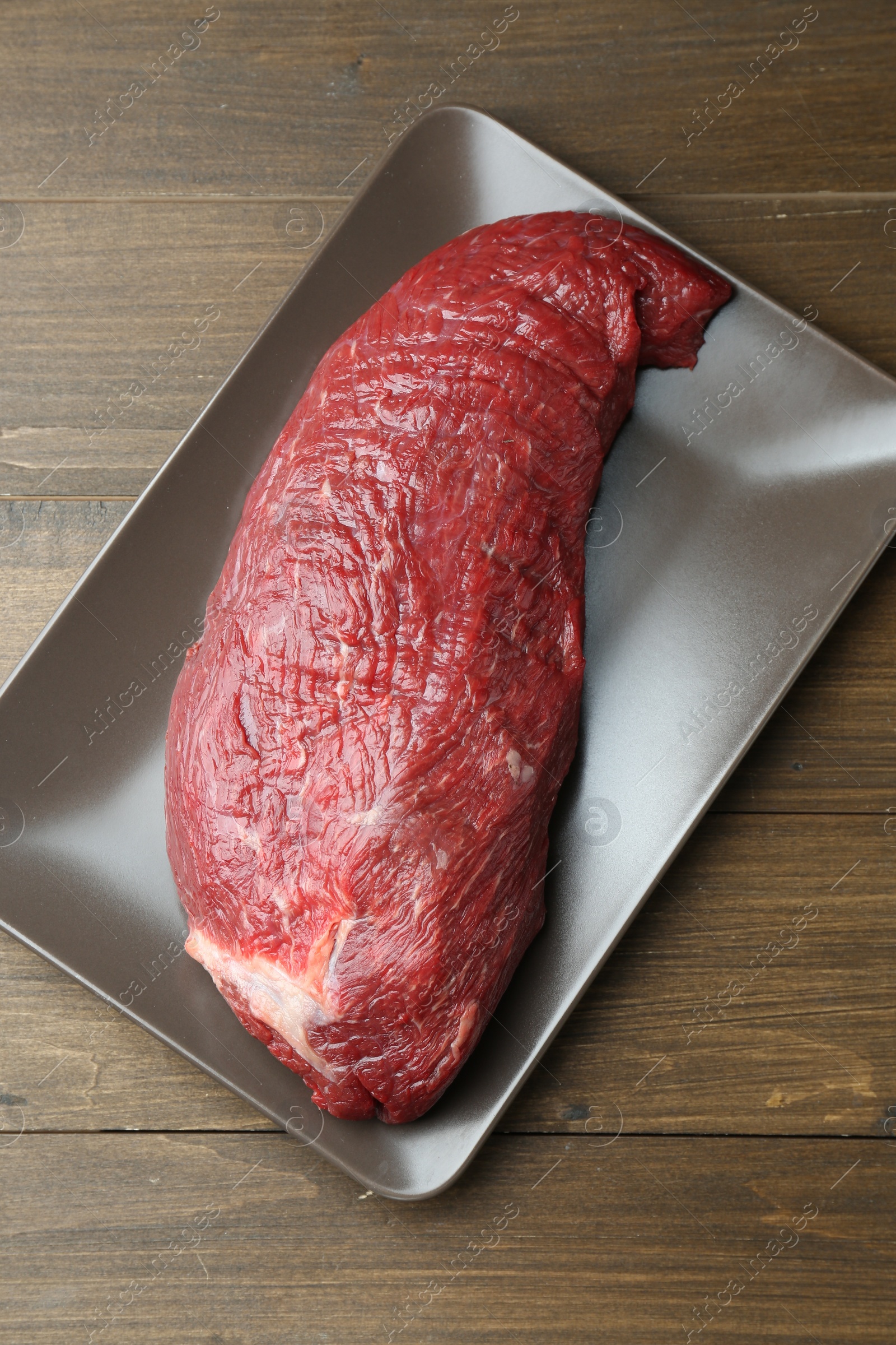 Photo of Plate with piece of raw meat on wooden table, top view