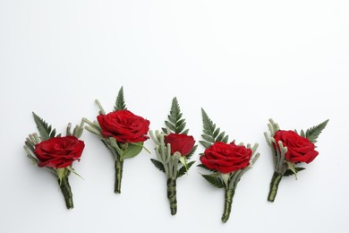 Many stylish red boutonnieres on white background, top view. Space for text