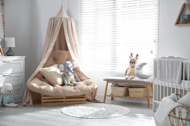 Photo of Beautiful baby room interior with comfortable armchair and bench near window