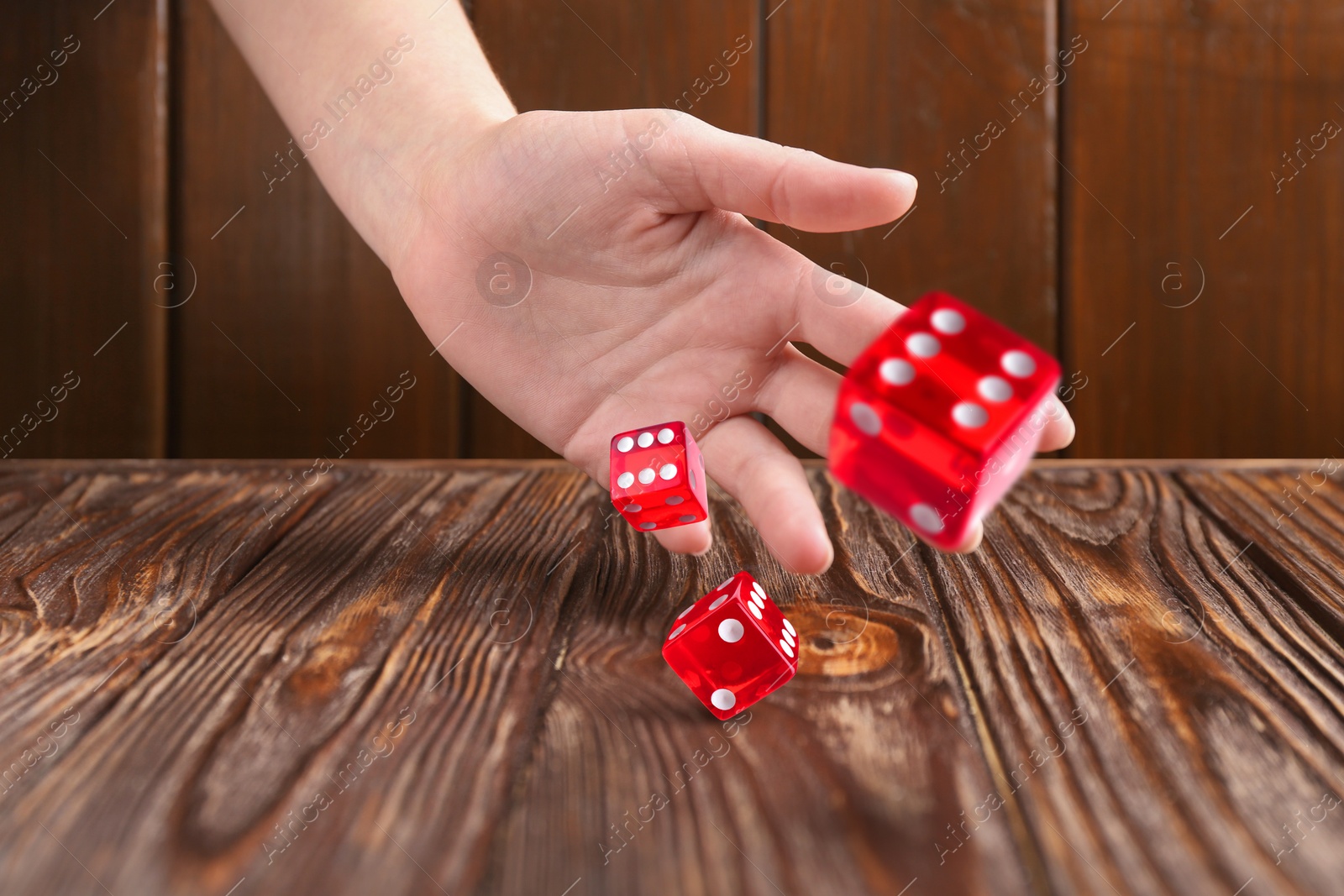 Image of Woman throwing red dice on wooden table, closeup