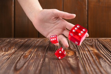 Woman throwing red dice on wooden table, closeup