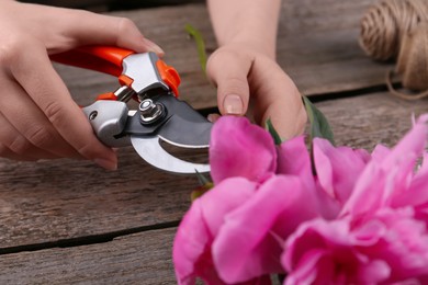 Photo of Woman trimming beautiful pink peonies with secateurs at wooden table, closeup