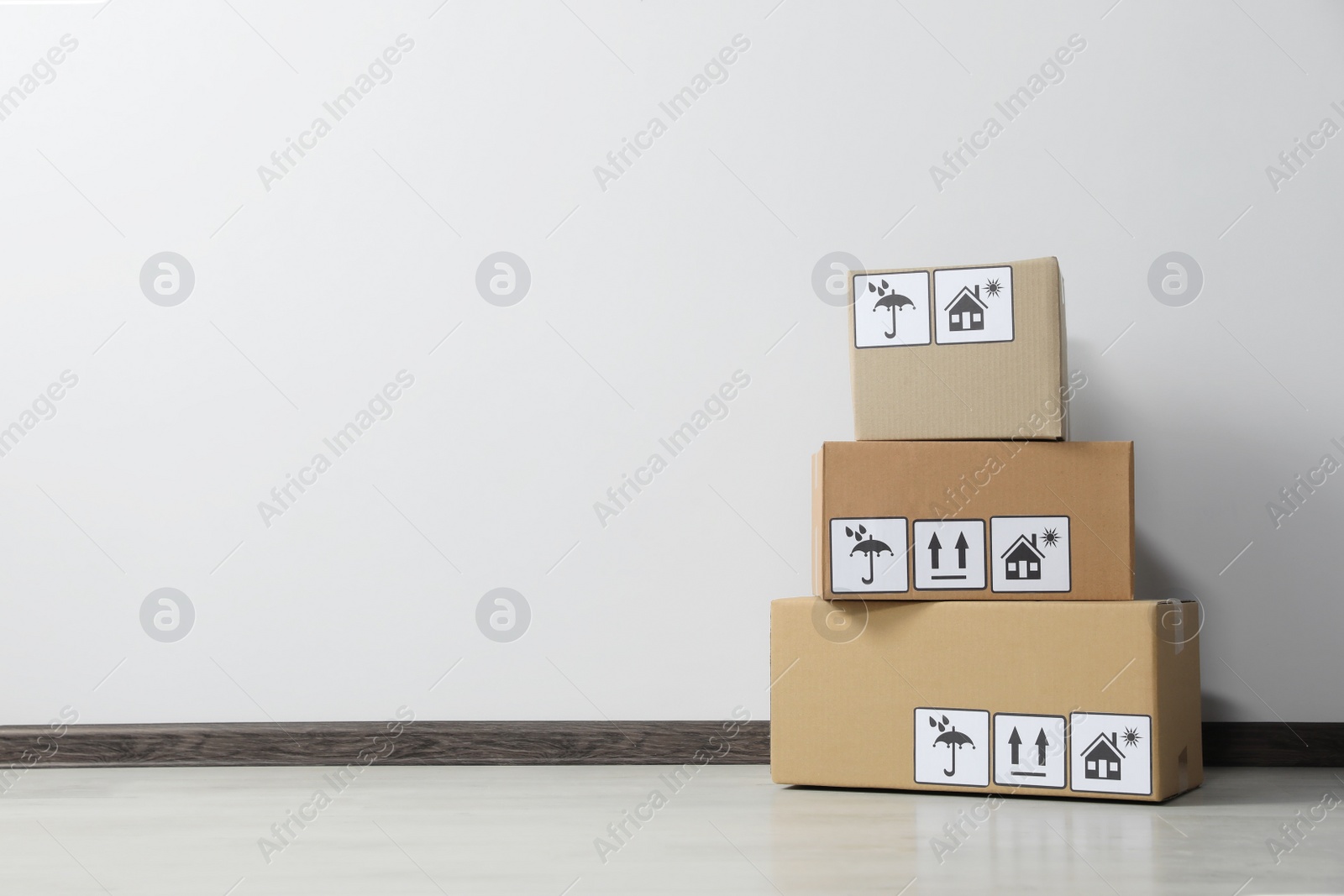 Photo of Many closed cardboard boxes with packaging symbols on floor near white wall, space for text. Delivery service