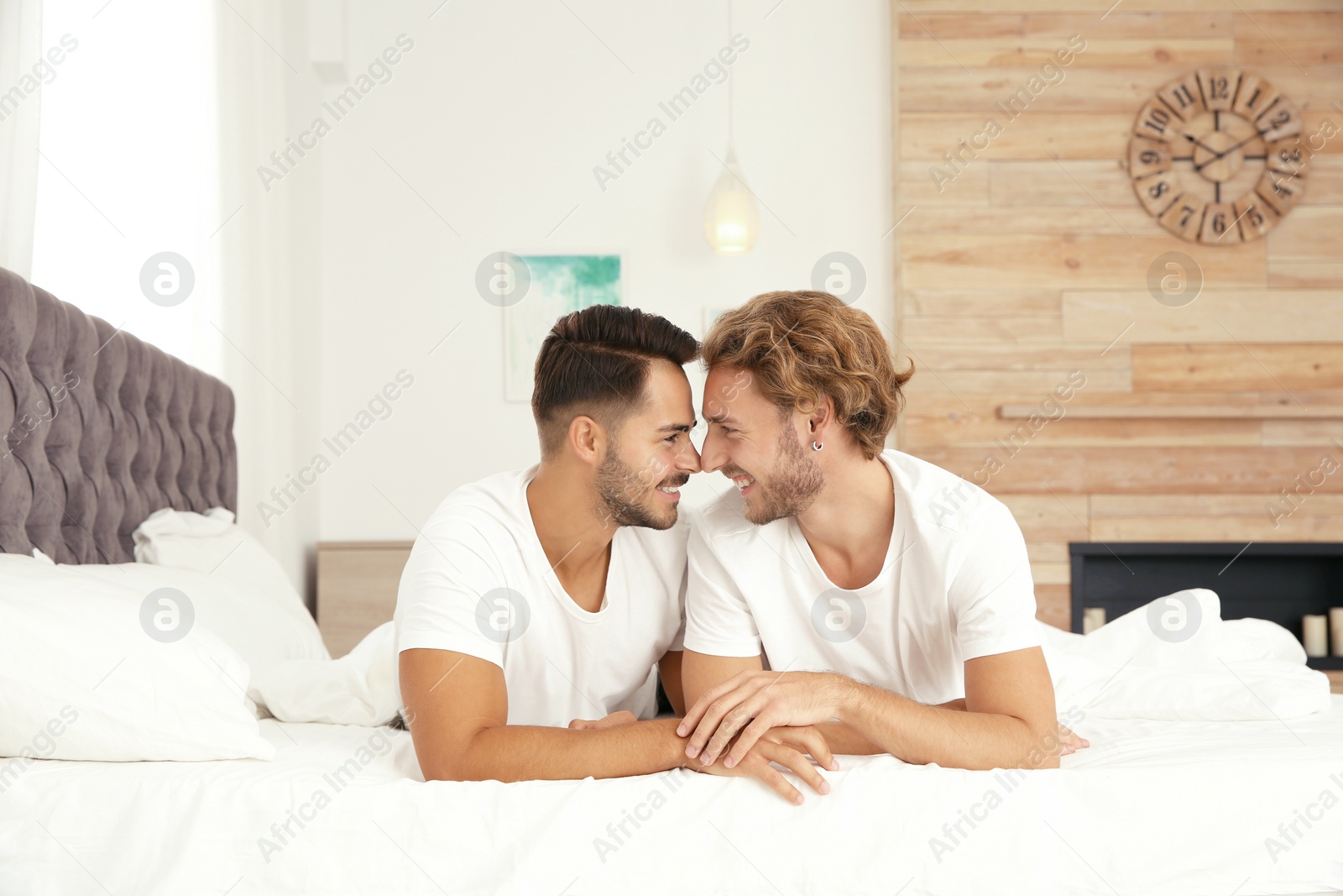 Photo of Happy gay couple lying on bed at home