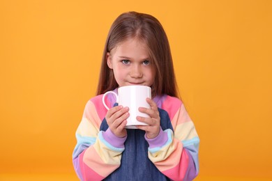 Photo of Cute girl drinking beverage from white ceramic mug on orange background