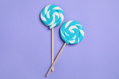 Sticks with bright lollipops on violet background, flat lay