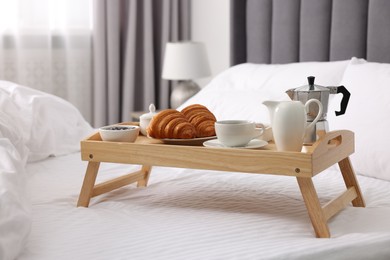 Photo of Wooden tray with tasty breakfast on bed at home
