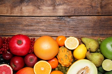 Many different fresh fruits and berries on wooden table, flat lay. Space for text