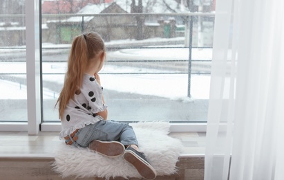 Lonely little girl sitting near window indoors. Autism concept