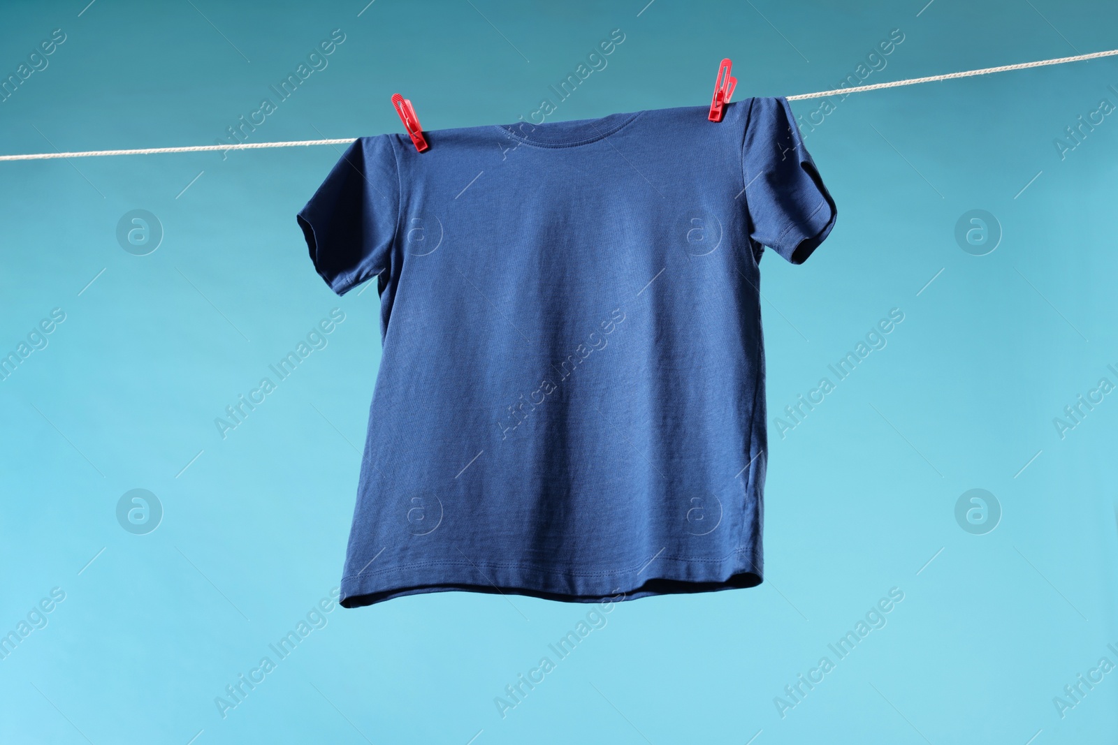 Photo of One t-shirt drying on washing line against light blue background