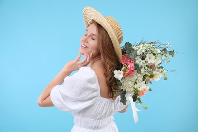 Photo of Beautiful woman in straw hat with bouquet of flowers on light blue background