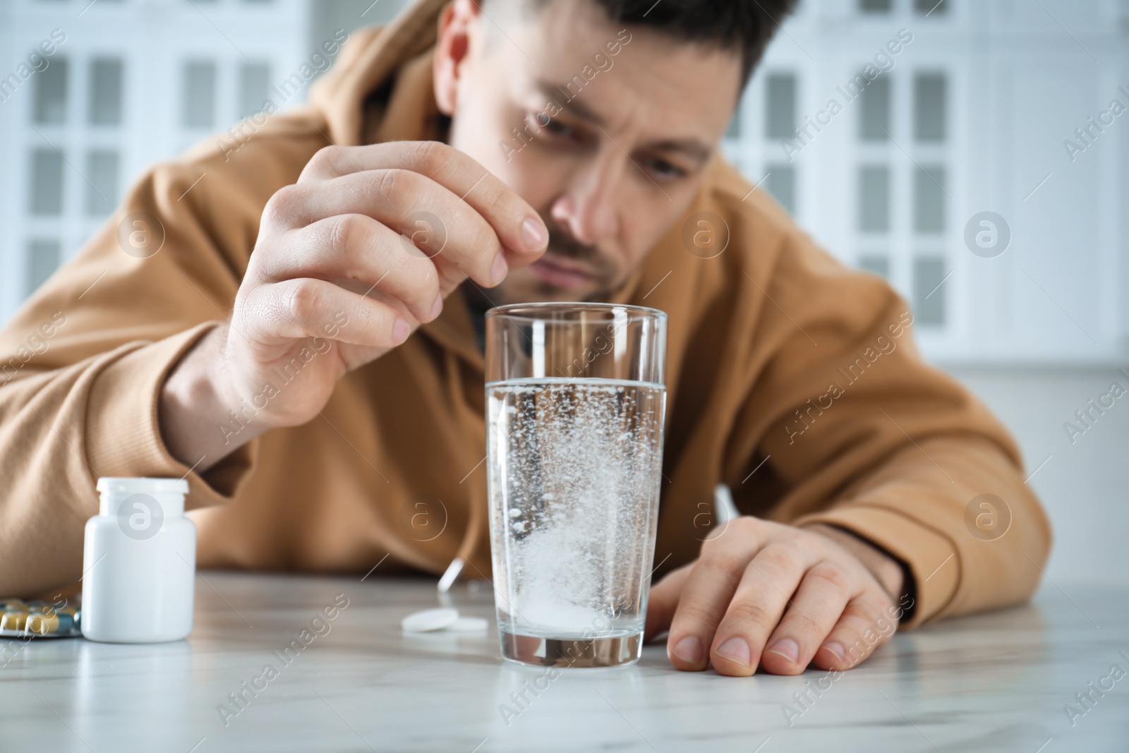 Photo of Man taking medicine for hangover at table in kitchen