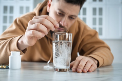 Man taking medicine for hangover at table in kitchen