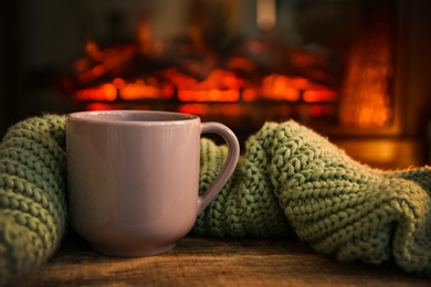 Cup with hot drink and knitted blanket on table against fireplace