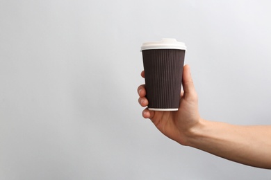 Man holding takeaway paper coffee cup on light background. Space for design